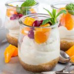 a tiny dessert glass with no-bake cheesecake topped with fresh oranges, cranberries and a mint leaf