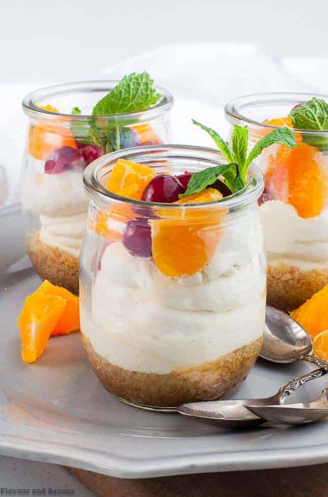 a tiny dessert glass with no-bake cheesecake topped with fresh oranges, cranberries and a mint leaf