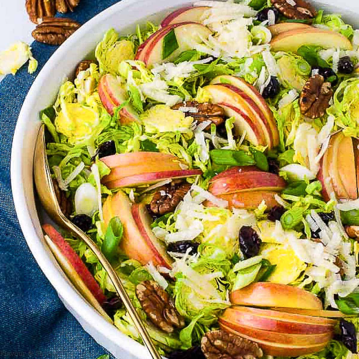 A bowl of shaved Brussels Sprout salad with sliced apples and pecans.