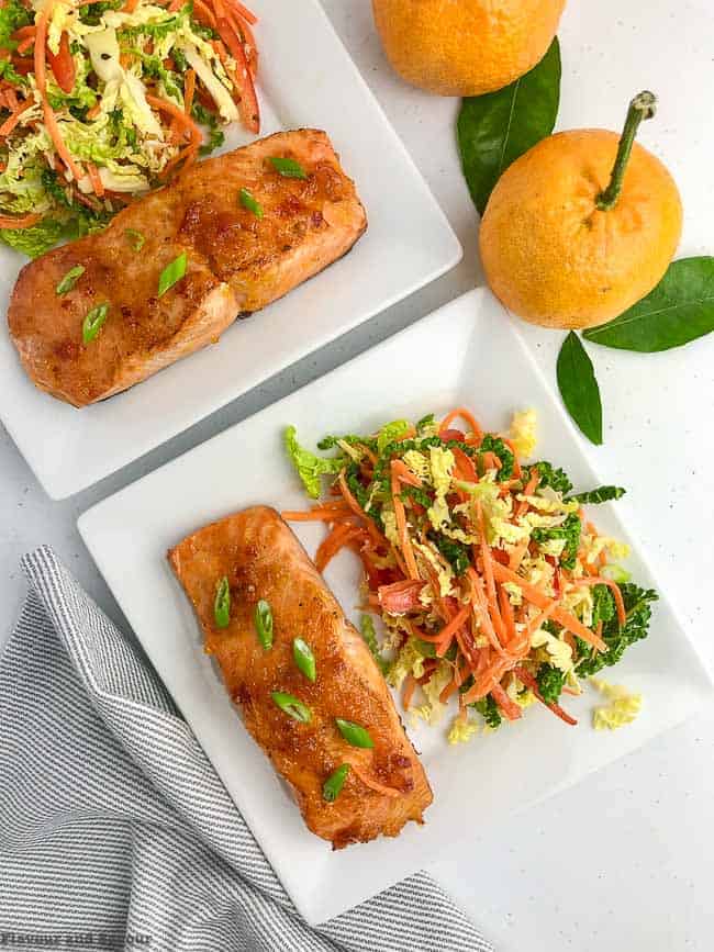 Citrus Glazed Baked Salmon with Sake on white plates with fresh oranges.