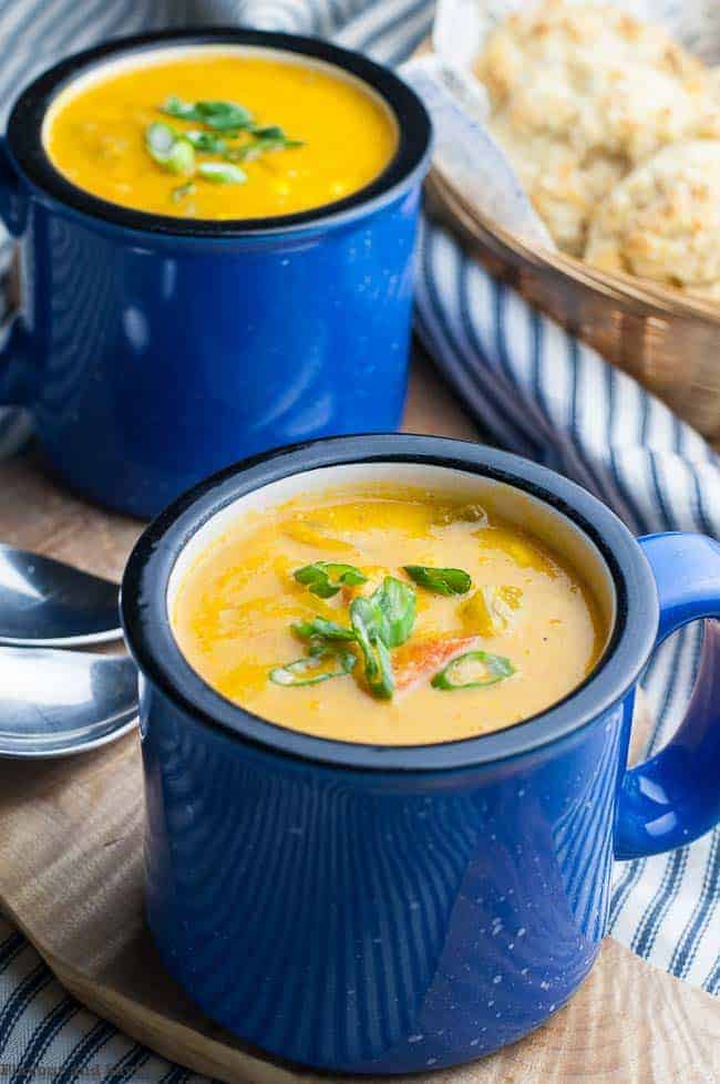 Two blue mugs of Sweet Potato Corn Chowder with baking powder biscuits in the background