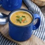 A blue mug filled with sweet potato corn chowder on a blue and white striped cloth