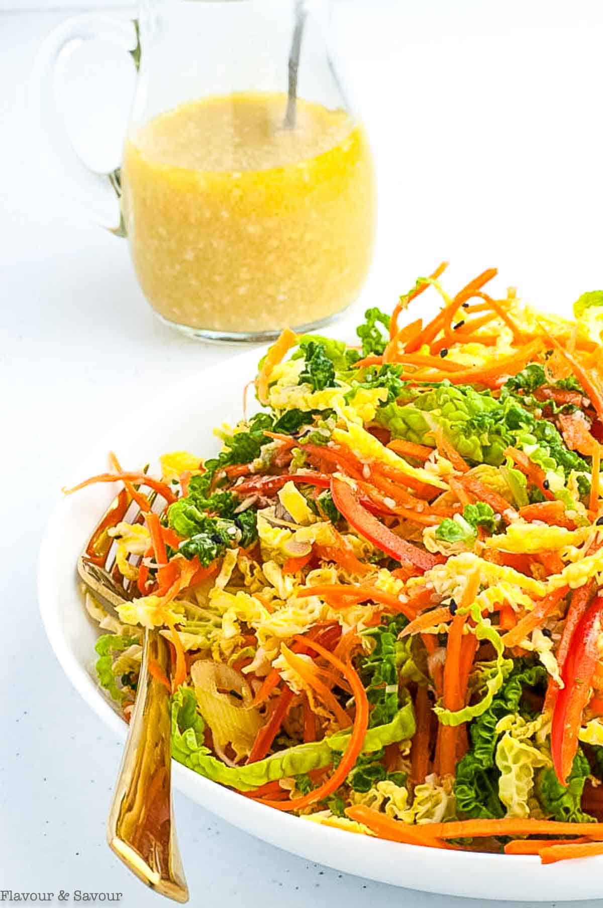 Side view of a bowl of cabbage coleslaw with a jar of dressing in the background.