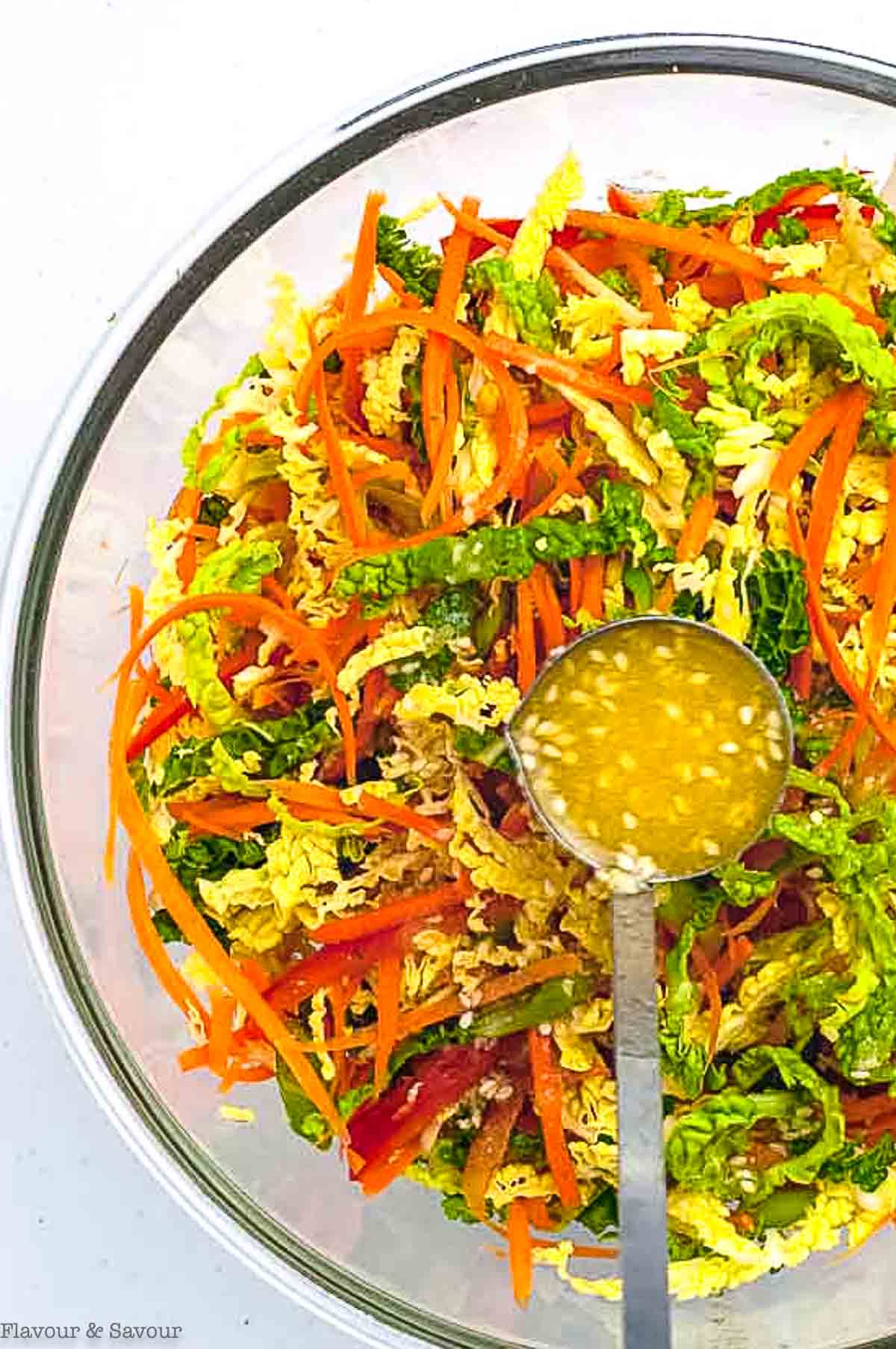 Overhead view of a glass bowl of cabbage coleslaw and a spoonful of sesame miso dressing.