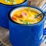 A soup mug of sweet potato corn chowder with a spoon in it.