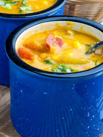 A soup mug of sweet potato corn chowder with a spoon in it.