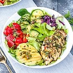 A bowl of chimichurri chicken salad with a sliced chicken breast, avocado and fresh veggies.