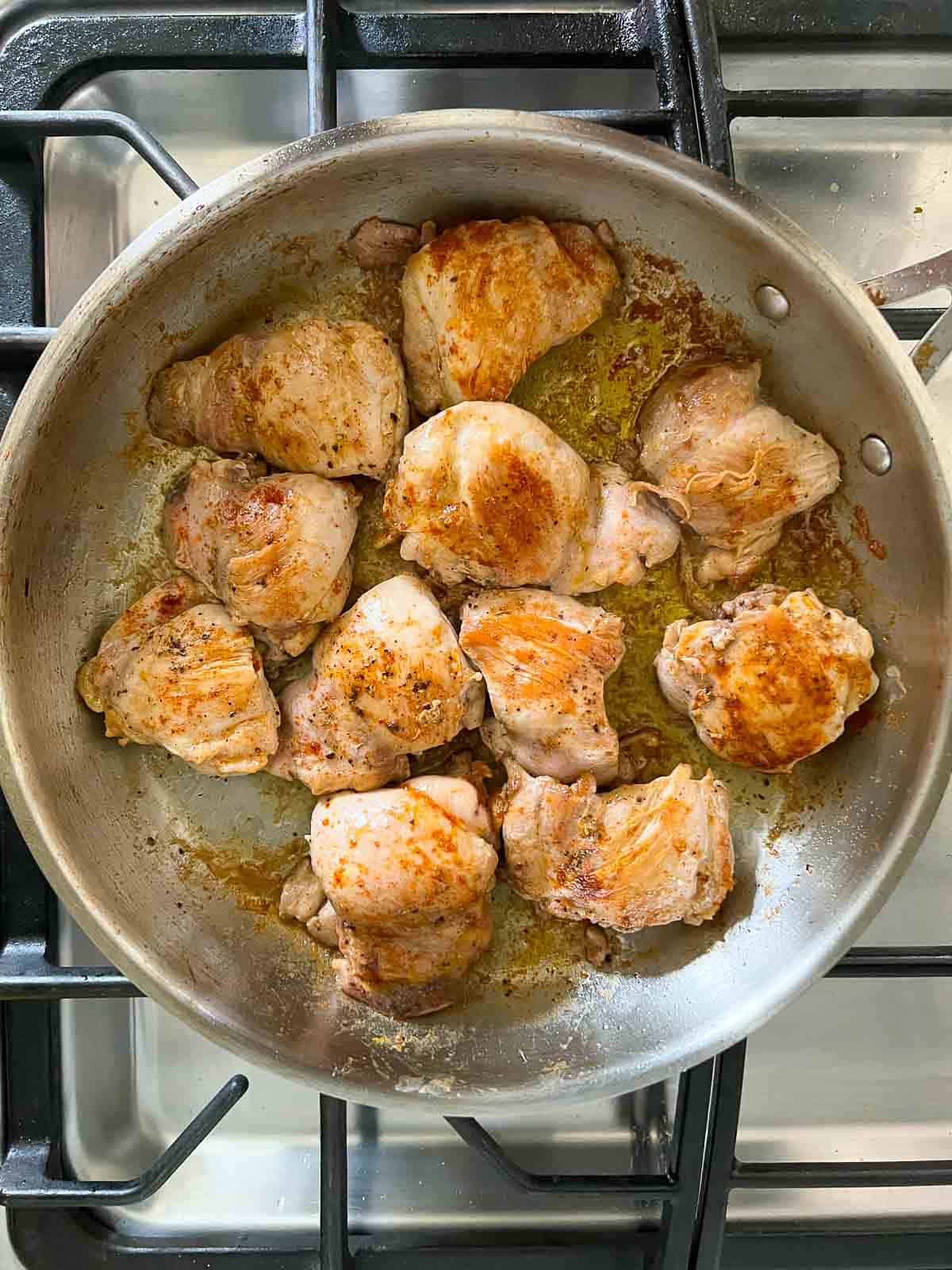 Browning chicken thighs in a skillet to make lemon artichoke chicken.
