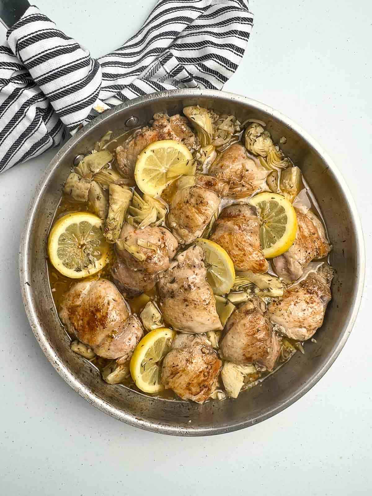 Adding the browned chicken thighs back into the lemon-artichoke sauce in a skillet.