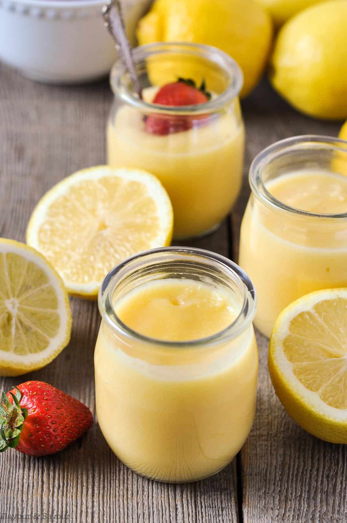 Small glass jars of Microwave Honey Lemon Curd with lemons and strawberries