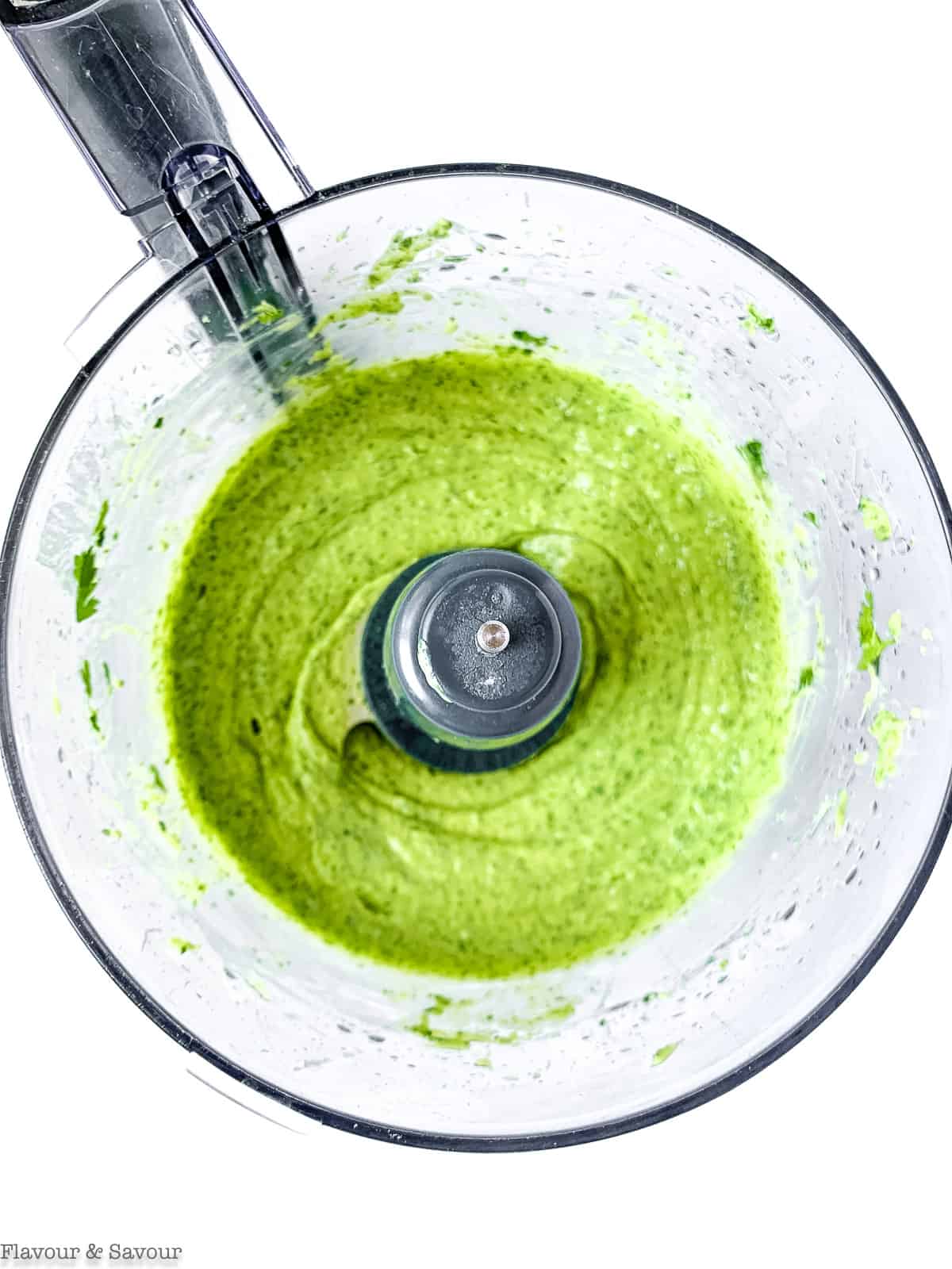 Avocado cream ingredients blended with oil in the bowl of a food processor.