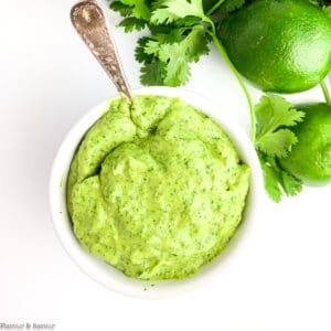 Overhead view of a small bowl of avocado cream sauce with lime and cilantro beside it.