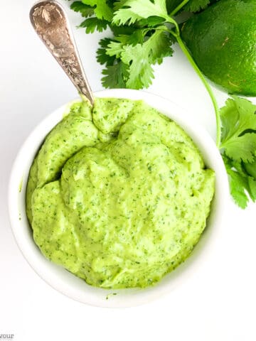 Overhead view of a small bowl of avocado cream sauce with lime and cilantro beside it.