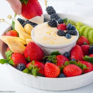 A hand dipping a strawberry into a small bowl of lemon curd fruit dip.