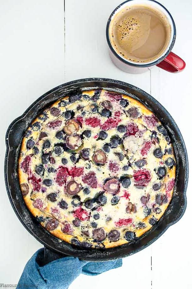 Cherry Berry Clafoutis in a skillet with a cup of coffee