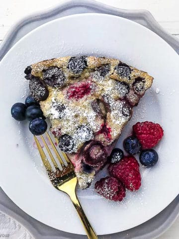 A slice of clafoutis on a white plate with a fork
