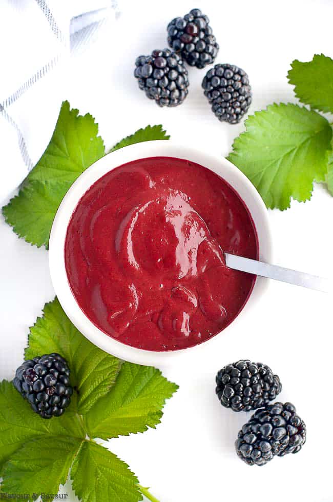 Overhead view of Blackberry Balsamic Dressing in a bowl surrounded by fresh blackberries and blackberry leaves