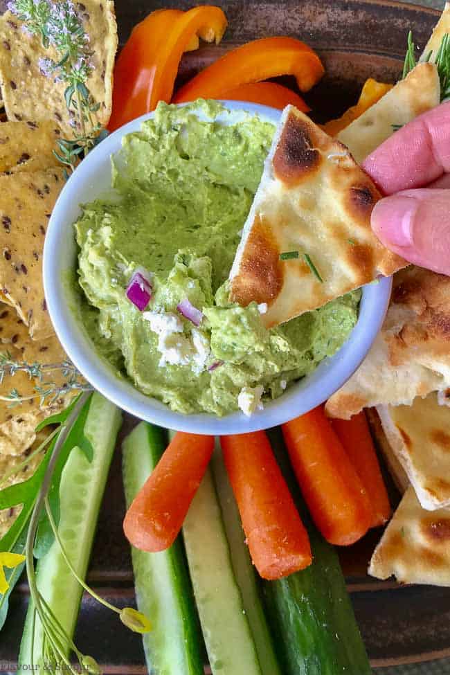 Dipping a pita chip into Avocado Feta Herbed Dip