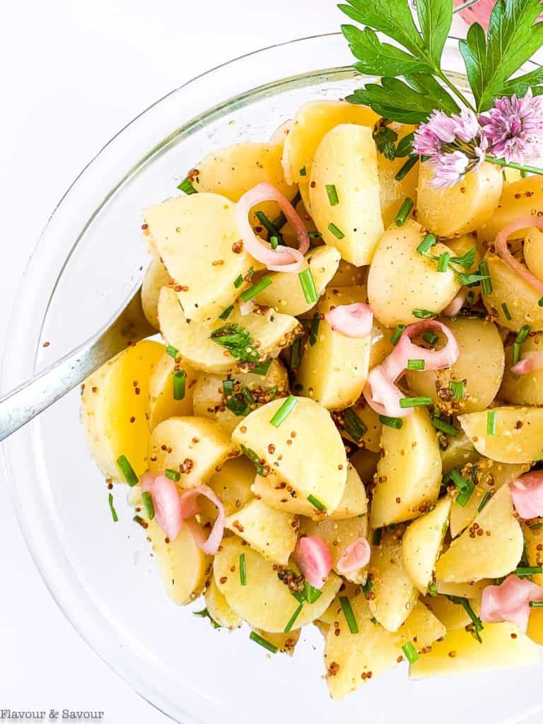 a glass bowl of Italian potato salad garnished with snipped chives, parsley and pickled shallots