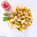 a glass bowl filled with Italian Potato Salad with a jar of pickled shallots beside it