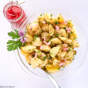 a glass bowl filled with Italian Potato Salad with a jar of pickled shallots beside it