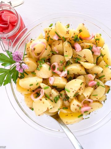 a glass bowl filled with Italian Potato Salad with a jar of pickled shallots beside it