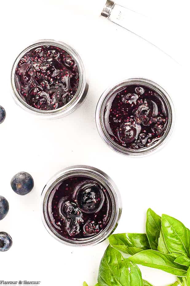 3 jars of blueberry basil chia seed jam with basil leaves beside