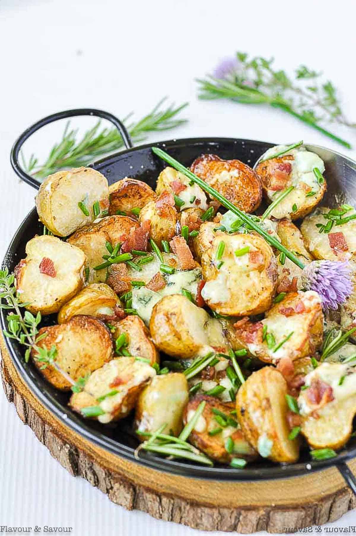 Close up view of grilled potatoes with blue cheese on a wood slab.