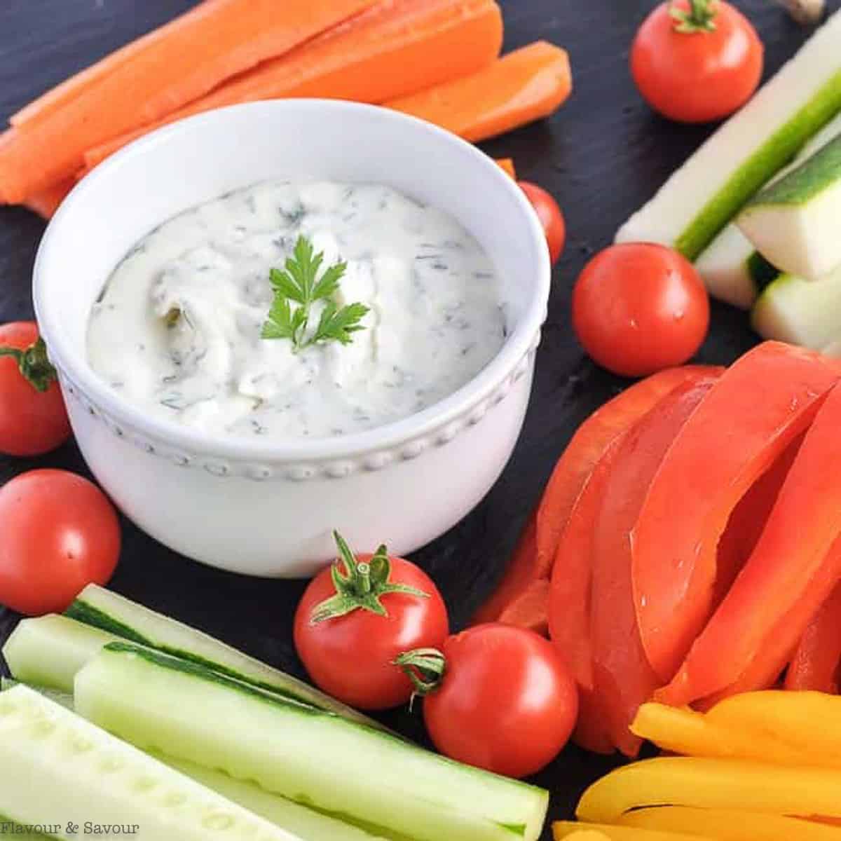 A bowl of herbed feta dip surrounded by fresh vegetable sticks.