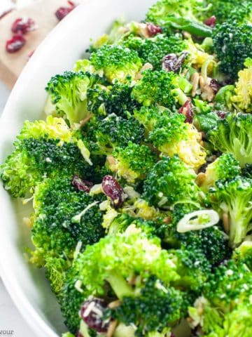a white bowl filled with honey-dijon broccoli salad with cranberries and sunflower seeds