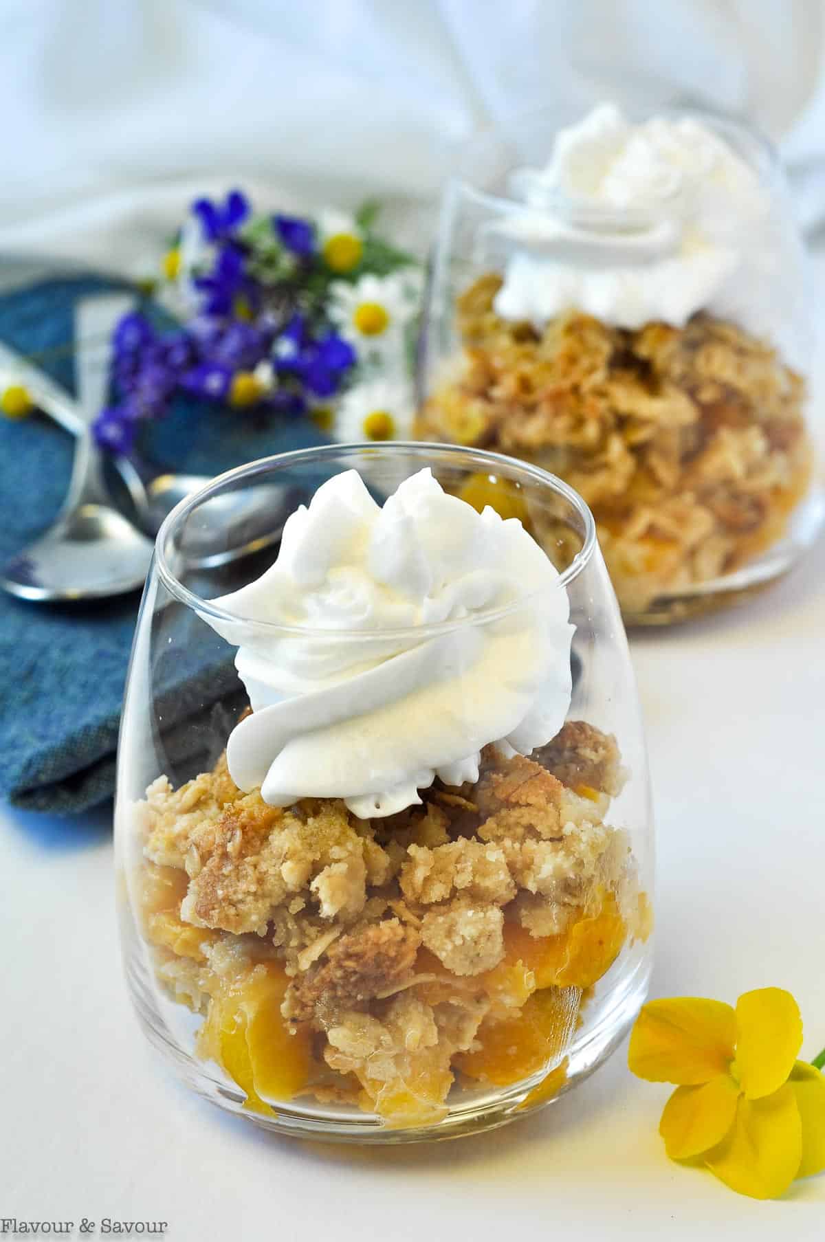 Peach Crisp with Bourbon and Vanilla in a clear glass dessert cup with whipped coconut milk