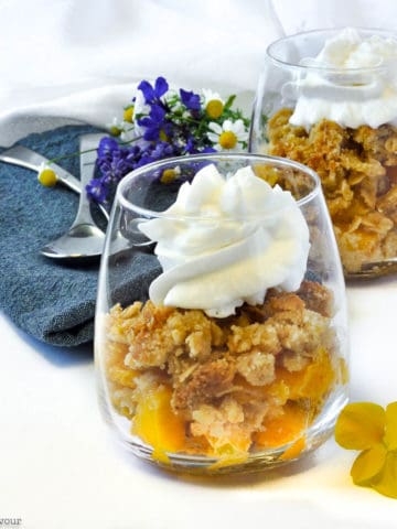Two dessert glasses with Peach Crisp and whipped coconut milk