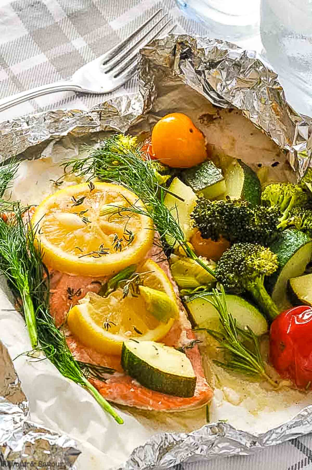 Close up view of a salmon fillet and vegetables in an opened foil packet.