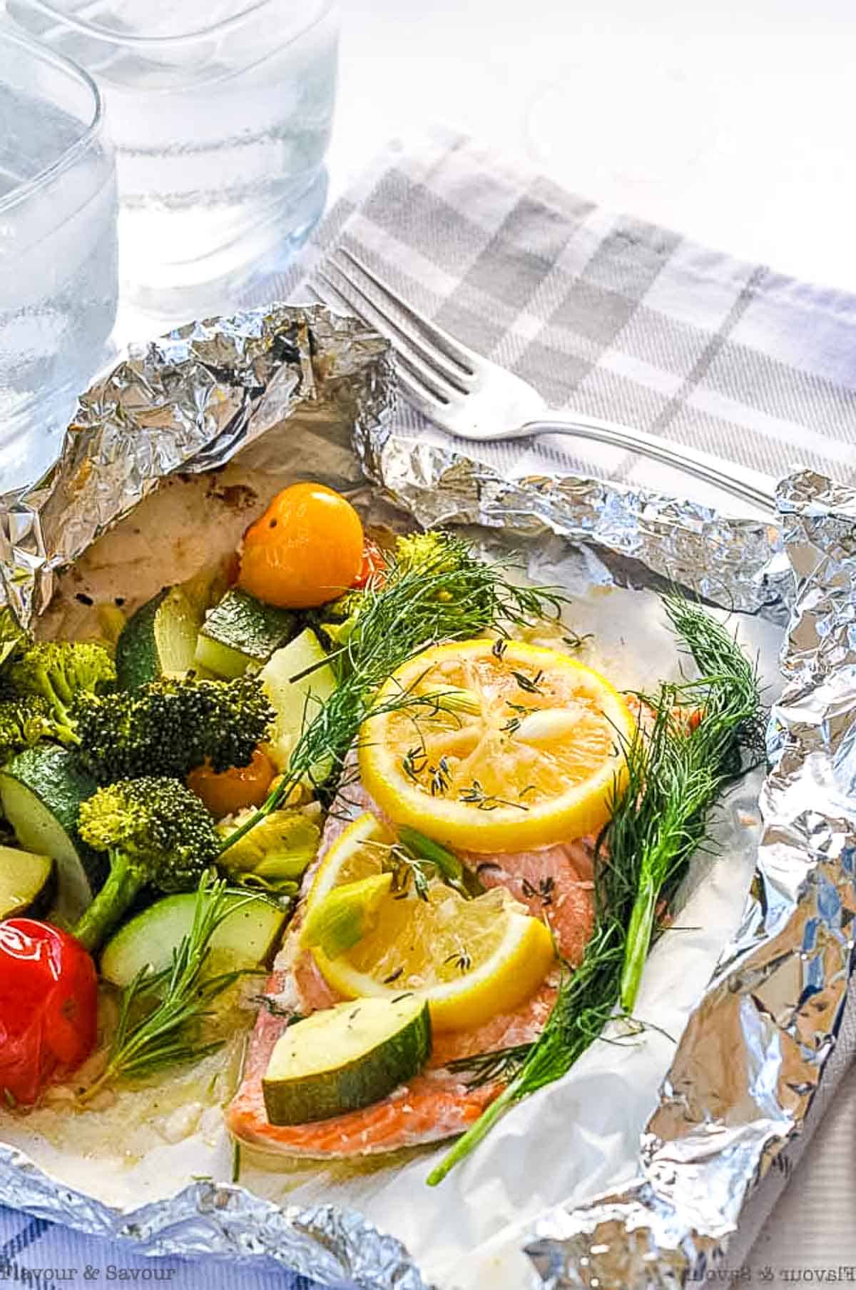 Wild salmon fillet with cooked vegetables and lemon slices in a foil packet.