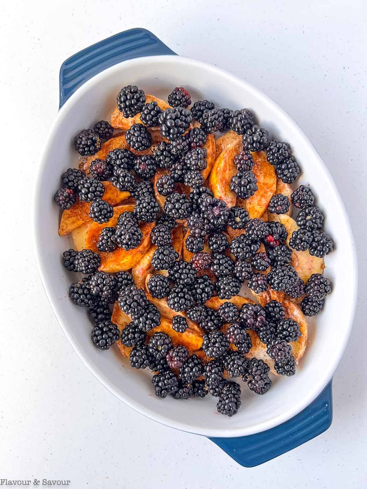 Blackberries on top of apple slices in a baking dish.