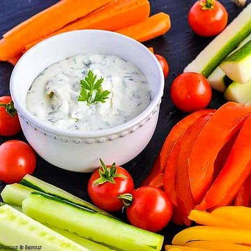 A bowl of herbed feta dip with lemon surrounded by fresh vegetables.