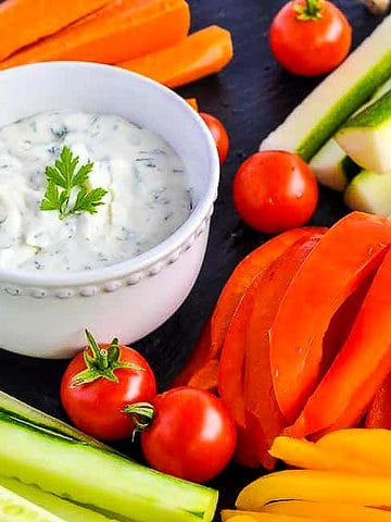 A bowl of herbed feta dip with lemon surrounded by fresh vegetables.