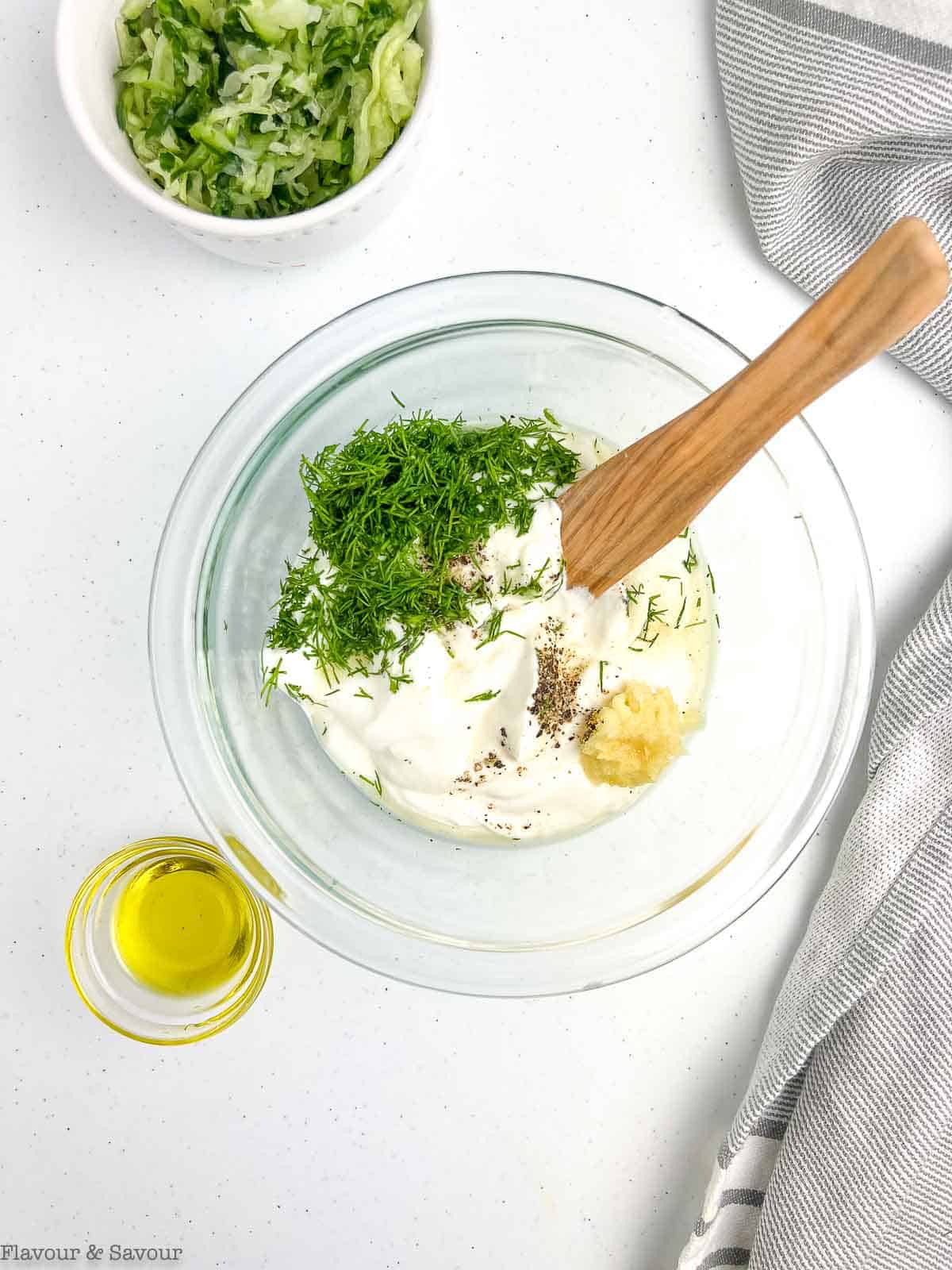 Combining ingredients for tzatziki sauce in a glass bowl.