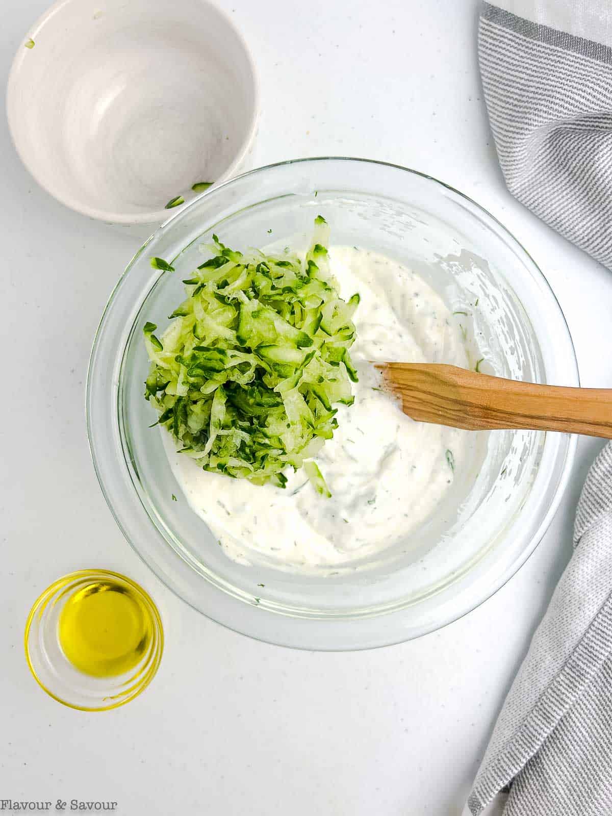 Grated cucumber added to a bowl of tzatziki.