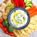 Greek tzatziki sauce in a bowl with fresh vegetables and naan bead.