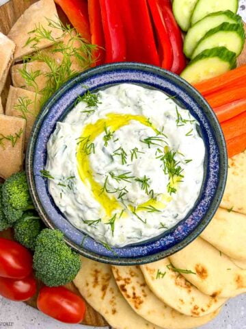 Greek tzatziki sauce in a bowl with fresh vegetables and naan bead.