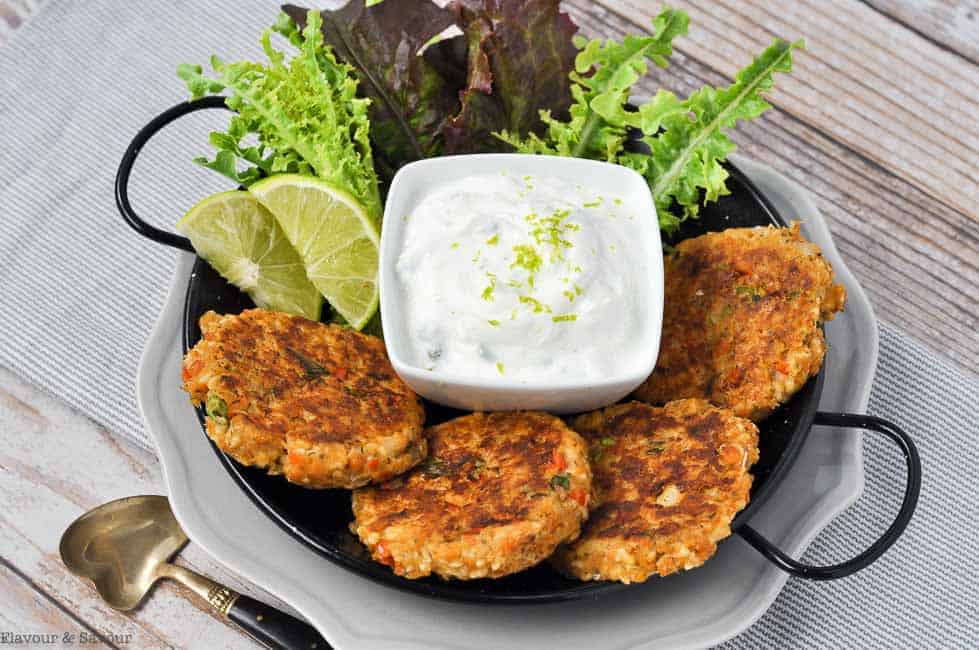 Four salmon patties on a plate with lime slices and dip