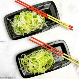 Two small black rectangular plates with chopsticks and apple pear slaw.