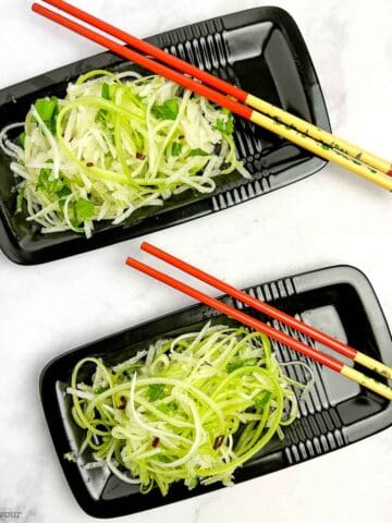 Two small black rectangular plates with chopsticks and apple pear slaw.