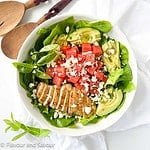 A bowl of greens with sliced chicken breast, watermelon cubes, avocado slices and feta cheese.