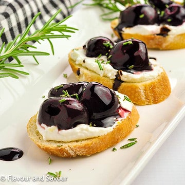 Three roasted cherry crostini with goat cheese on a white serving platter.