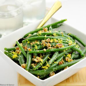 A bowl of Parmesan Green Beans with pecans in a square bowl with a spoon.