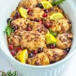 A serving bowl with chicken thighs baked with cranberries and rosemary.