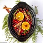 Simmering holiday potpourri spice mix in a slow cooker bowl with cedar boughs.