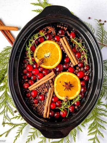 Simmering holiday potpourri spice mix in a slow cooker bowl with cedar boughs.